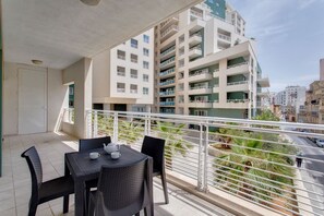 A balcony with a table and chairs, overlooking a residential area with multi-story buildings.