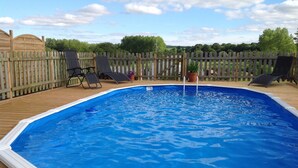 Una piscina sobre terra amb una terrassa de fusta, envoltada d'una tanca de fusta i plantes en testos.