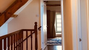 Una escala de fusta que condueix a una habitació amb un sostre inclinat i una porta ben visible al final.