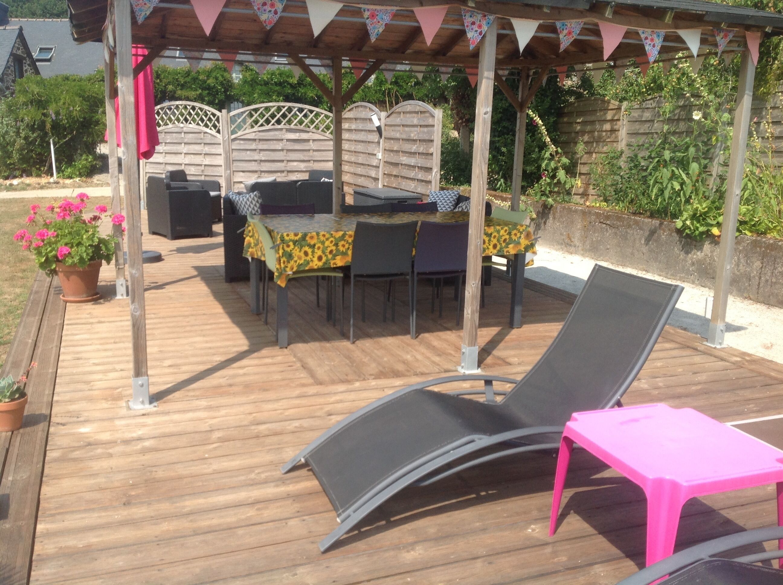 An outdoor patio with a wooden deck, a covered seating area with tables and chairs, and a pergola with triangular flags.