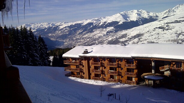 Eine Holzhütte mit Balkonen, umgeben von schneebedeckten Bergen und Bäumen.