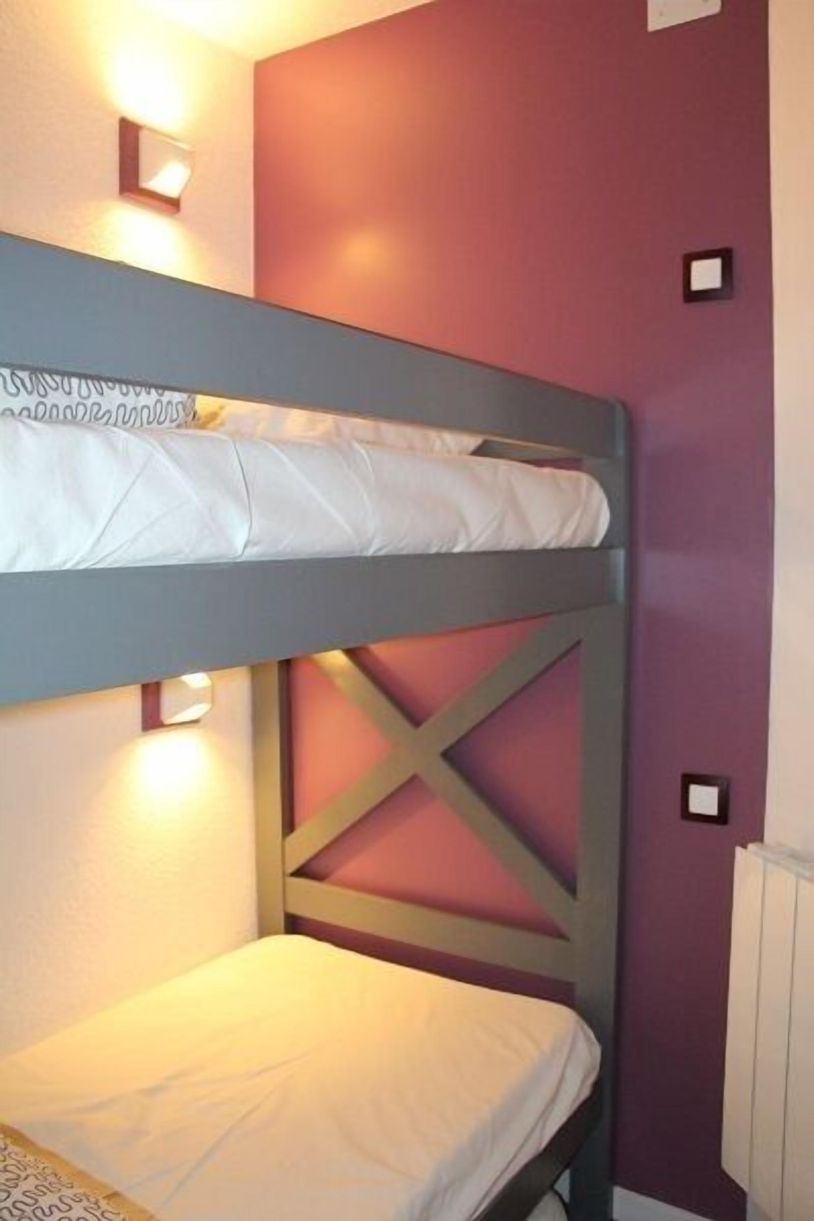 Un lit superposé avec une structure renforcée en croisillons, deux lampes fixées au mur et un radiateur.