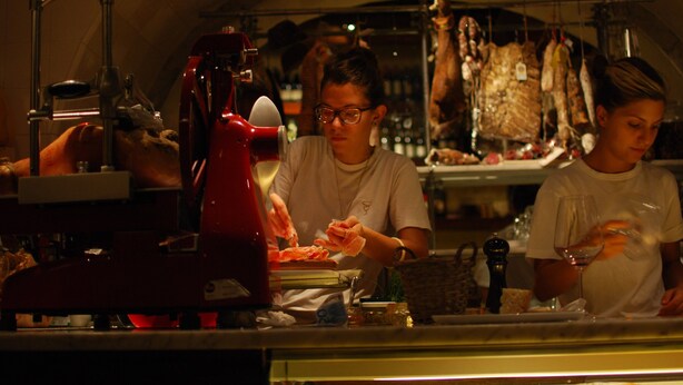 Un espace cuisine avec un appareil électroménager rouge, une présentation de viande suspendue et une personne qui travaille.