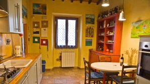 Une cuisine équipée d’une cuisinière, d’un évier et d’une table à manger avec des chaises. On y trouve différents placards de cuisine et une fenêtre avec des rideaux.