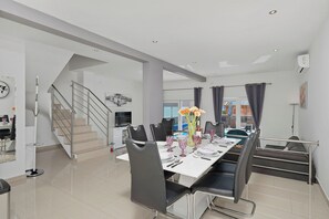 Un espace de salle à manger moderne avec une table blanche dressée pour six personnes, des chaises noires et un escalier menant à un niveau supérieur.