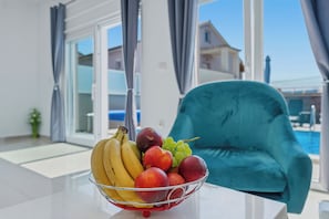 A room with a teal armchair, a glass door leading to a pool, and a fruit bowl on a table. - Holiday house "Sabine pink"  (Skrpčići)