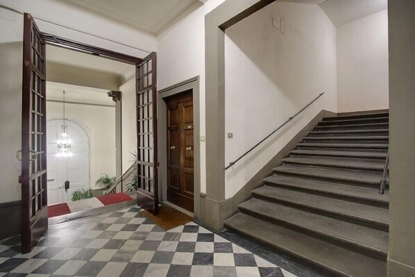 Una escalera con barandilla, piso a cuadros y una puerta con panel de vidrio.