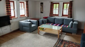 A living room with a sofa, a coffee table, a television, and plaid curtains. - Franconian half-timbered house for 5 people (Krombach)