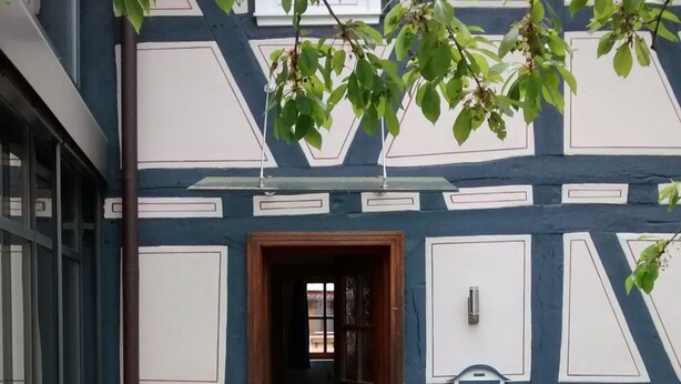 A building with a dark facade and white trim, a wooden door, and a small mailbox on the wall. - Franconian half-timbered house for 5 people (Krombach)