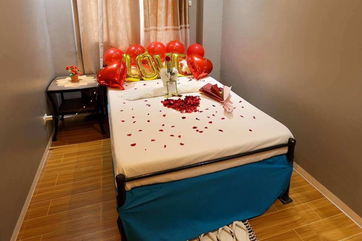 A hotel room with a bed, a small table with a flower vase, and a window with curtains.