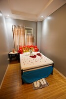 A hotel room with a bed, a small table with a flower vase, and a window with curtains.