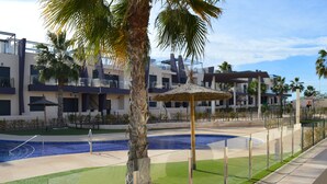 Een modern hotel met een zwembad, palmbomen en een rieten parasol.