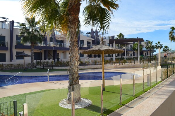 A modern hotel with a swimming pool, palm trees, and a thatched umbrella.
