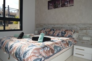 A bedroom with a bed, a nightstand, a window, and a cityscape painting on the wall. - Torre de la Horadada Elisa Costa Beach (Torre de la Horadada)