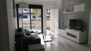 Een moderne woonkamer met een bank, voetenbankje en een flatscreen televisie op een witte kast.