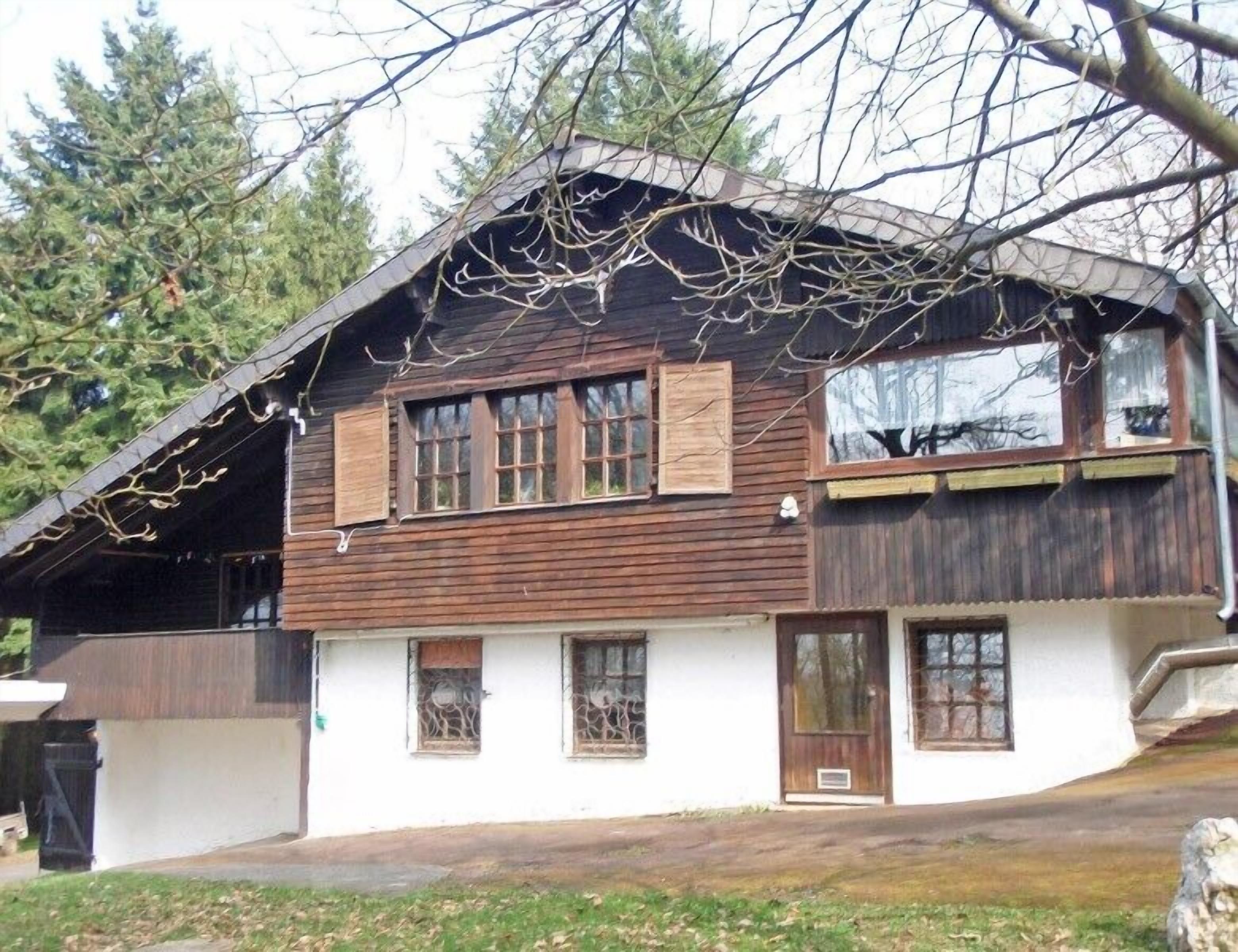 Uma casa de madeira de dois andares, com telhado inclinado, várias janelas e uma chaminé visível.
