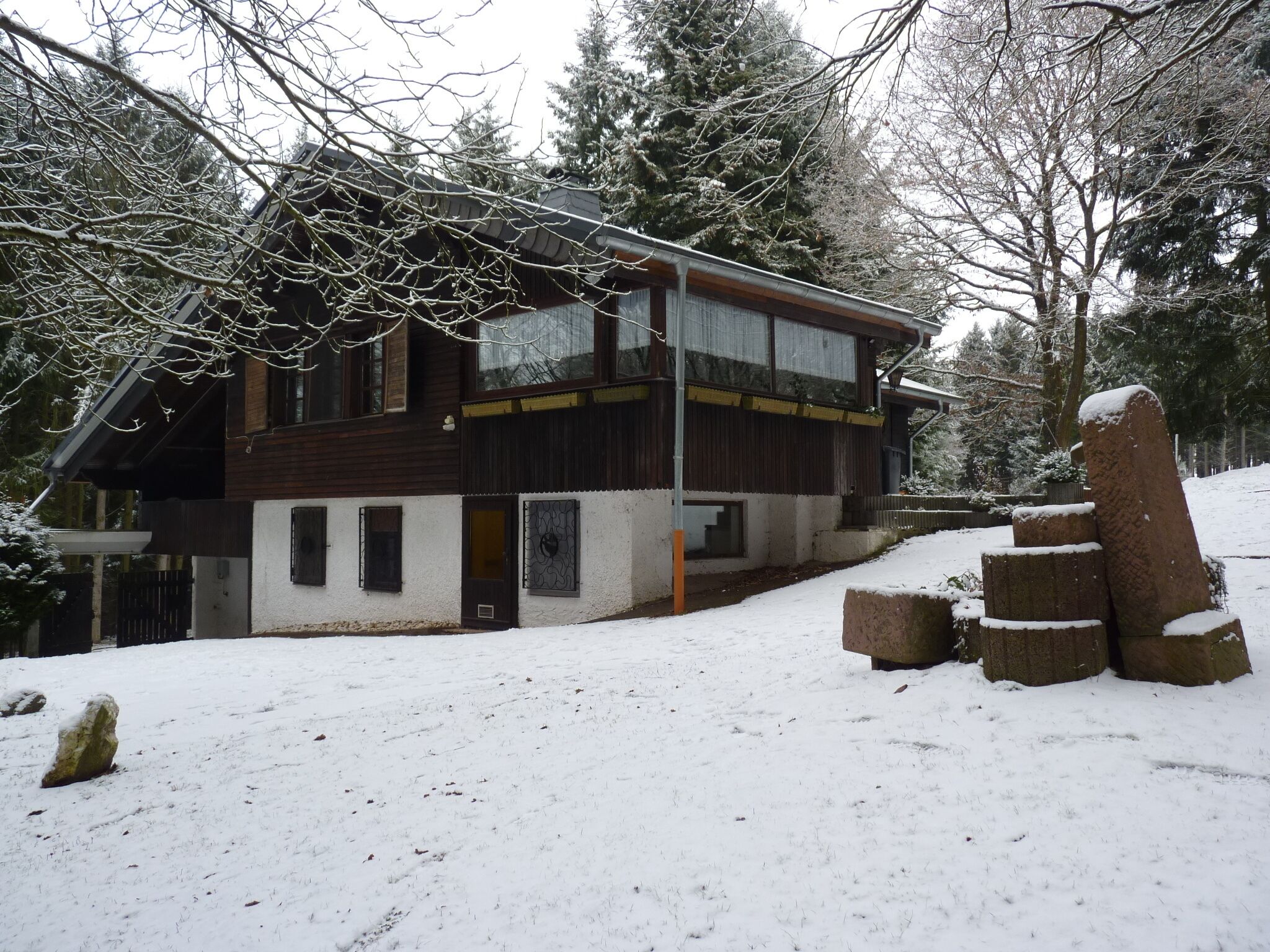A two-story wooden cabin with a snow-covered landscape, surrounded by trees.