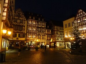 Una plaza tradicional europea iluminada de noche, con edificios históricos de entramado y adornos navideños, y calles empedradas.