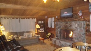A cozy cabin interior with a stone fireplace, leather recliner, wooden dining table, and a television displaying Netflix.