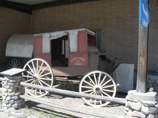 Une charrette à cheval, immobile, avec de grandes roues, est garée devant un bâtiment en briques sur lequel on peut lire une pancarte indiquant : « Service postal américain : Salmon à Forney, via Leesburg ».