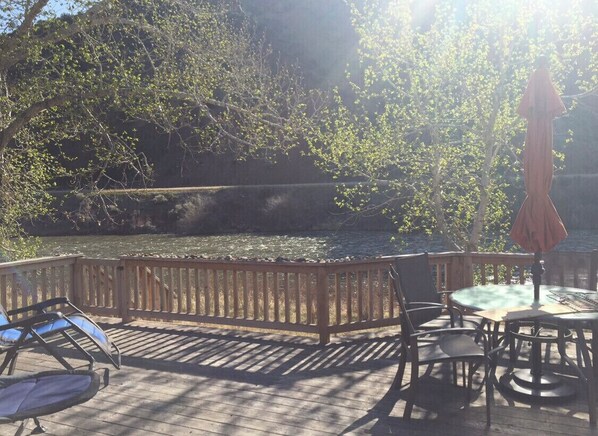 A wooden deck with outdoor furniture, including chairs and a table, overlooking a body of water. - Comfy, charming cabin on the Salmon River a few miles from Gold Bug Hot Springs (Salmon)