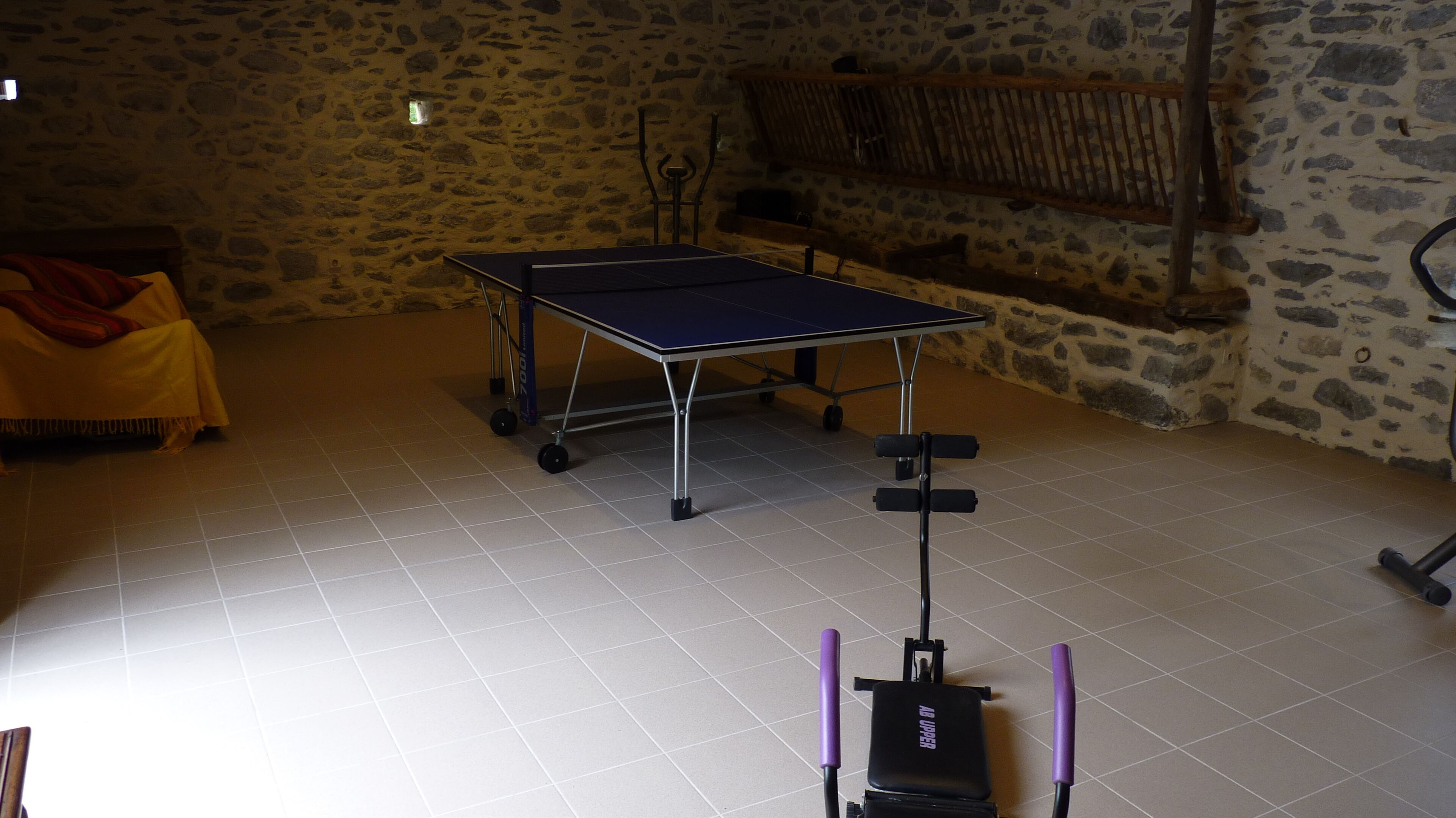A ping pong table in a room with stone walls and tiled flooring.