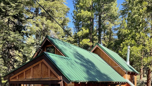 Una cabaña de madera con techo verde, rodeada de árboles.