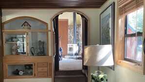 Una sala de estar acogedora con techo de madera, un sofá, una lámpara y vista a una chimenea de piedra a través de una puerta abierta.