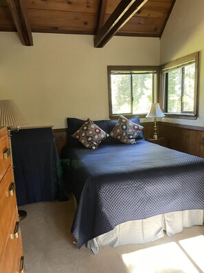 Une chambre à coucher avec un lit, deux oreillers, une table de chevet, une lampe, une fenêtre et une commode en bois.