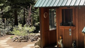 Una cabaña rústica de madera con techo de metal, rodeada por un sendero de piedra y vegetación natural.