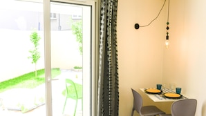 Et spiseområde med et bord dækket til to personer, to stole, et vindue med gardiner og en lampe.