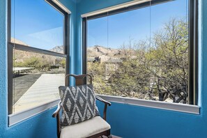 A room with a large window, a chair with a patterned cushion, and a view of a desert landscape. - Gorgeous Mountain & City Views, Pools, & Hot Tubs (Tucson)