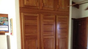 Quarto com guarda-roupa de madeira, cama com colcha florida e cadeira de madeira.