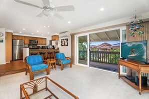 A spacious living area with a kitchen, bar stools, a television, and a balcony with a view of houses. - Spacious 2BR/2BA Condo - Ocean View, Above it All, Oceanside Pool and 3 Zone A/C (Kailua-Kona)