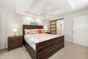 Quarto com cama de madeira, duas mesas de cabeceira, ventilador de teto e uma janela grande.