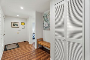 Un pasillo con suelo de madera, un banco y una puerta con paneles verticales.