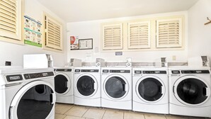 A laundry facility with multiple washing machines, a control panel, and informational posters on the wall.