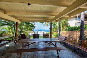 Une terrasse extérieure couverte, dotée de tables de pique-nique et de bancs, offrant une vue sur une piscine et l’océan.