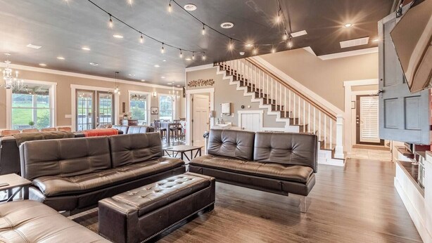 A spacious living room with leather sofas, a dining area, and a staircase leading to a second floor.
