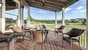 A covered deck with wicker furniture, a grill, and a view of a green landscape.