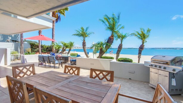 Un patio exterior con una mesa y sillas de madera, una parrilla y un paraguas rojo.