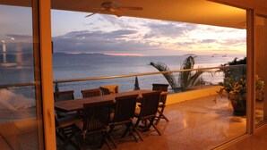 A balcony with a table and chairs, overlooking the ocean and a sunset. - Best value !! Luxury Beach Front Condo (Emiliano Zapata)