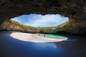 Ein Strand mit klarem türkisblauem Wasser, einem Sandufer und dem Eingang zu einer Höhle.