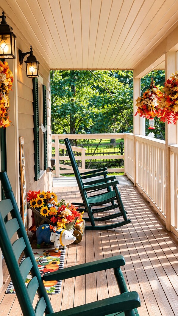 A covered porch with wooden railings, rocking chairs, and a flower arrangement.