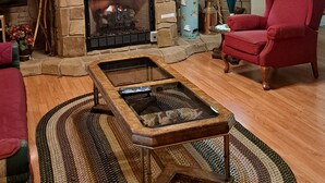 A cozy living room with a stone fireplace, a wooden coffee table, and a red armchair.