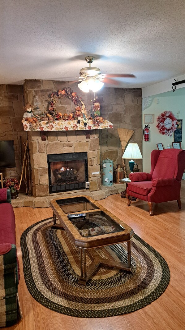 A cozy living room with a stone fireplace, a wooden coffee table, and a red armchair.