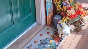 A green door with a wreath, a 'WELCOME' sign, and a porch decorated with autumn-themed items.