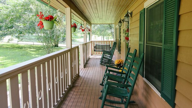 A covered porch with wooden railings, green rocking chairs, and hanging flower baskets.