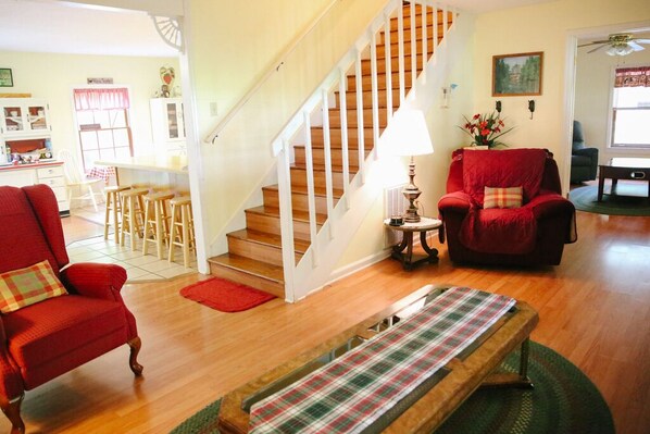 A cozy living room with a wooden staircase, a red armchair, a plaid bench, and a dining area with a table and chairs. - FARM ANIMALS: RESCUES, Mini HORSES and mini DONKEYs; (Sevierville)