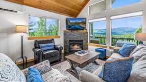 A cozy living room with a fireplace, leather sofa, and large windows offering scenic mountain views. - 1PM In/Out + Pool Access | Scenic Mountain Cabin Built for More Family Time (Ronald)